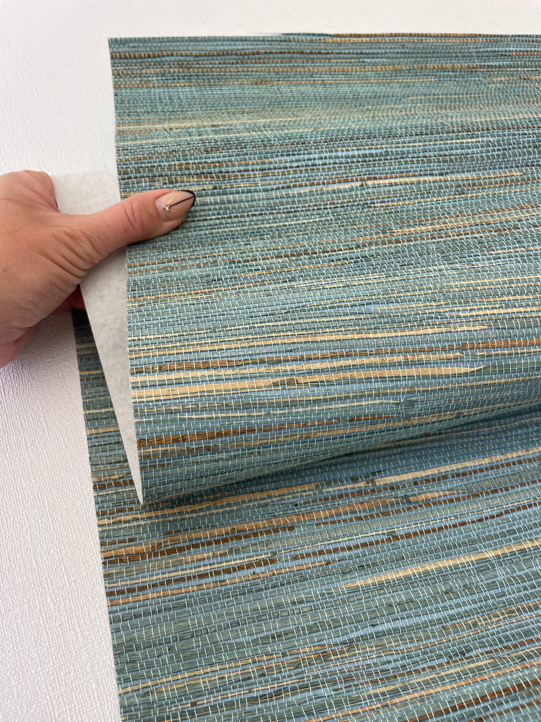 hand holding natural grasscloth wallpaper sample showing woven fiber texture and natural wallcovering material