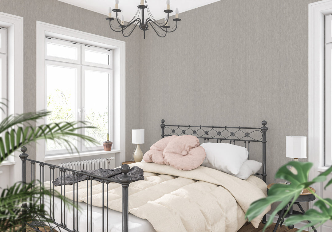 Light greige faux linen wallpaper with a subtle woven texture in a bright bedroom featuring a black metal bed frame, cream bedding, and white window trim.
