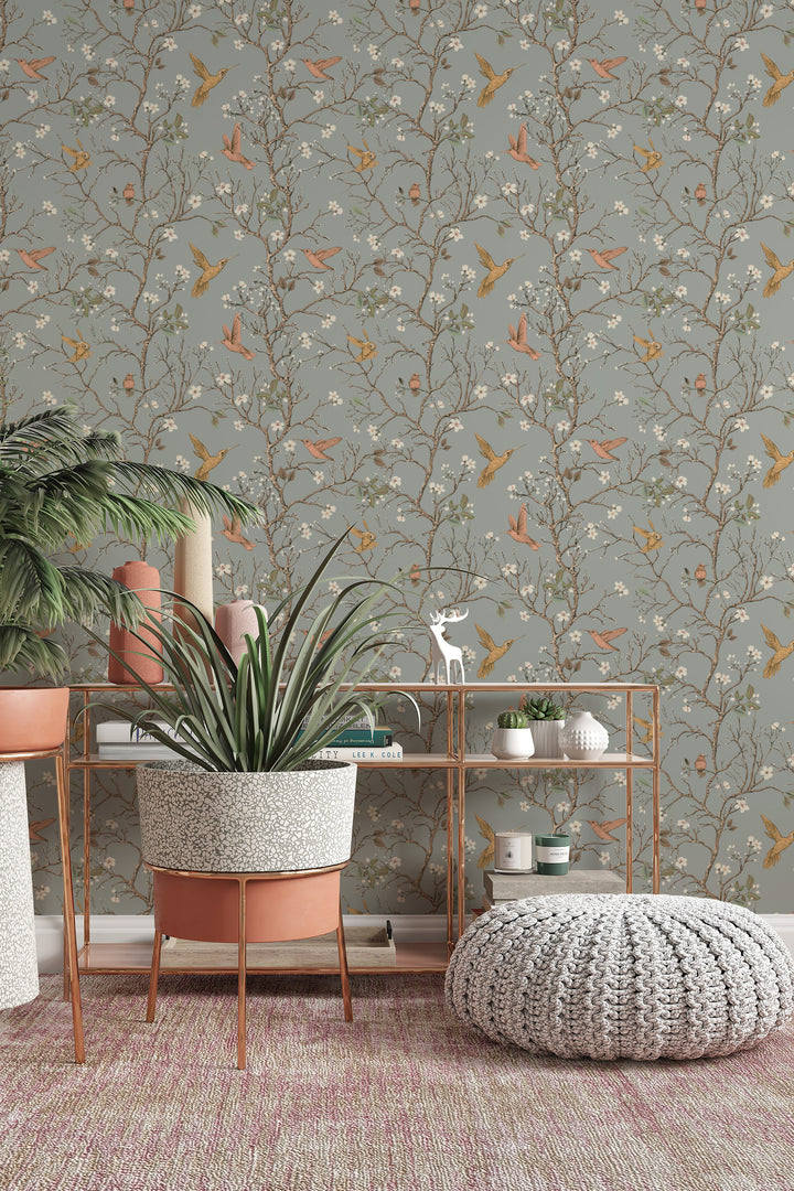 Sage gray hummingbird wallpaper with flowering branches and colorful birds featured as an accent wall behind a plant stand and modern decor.