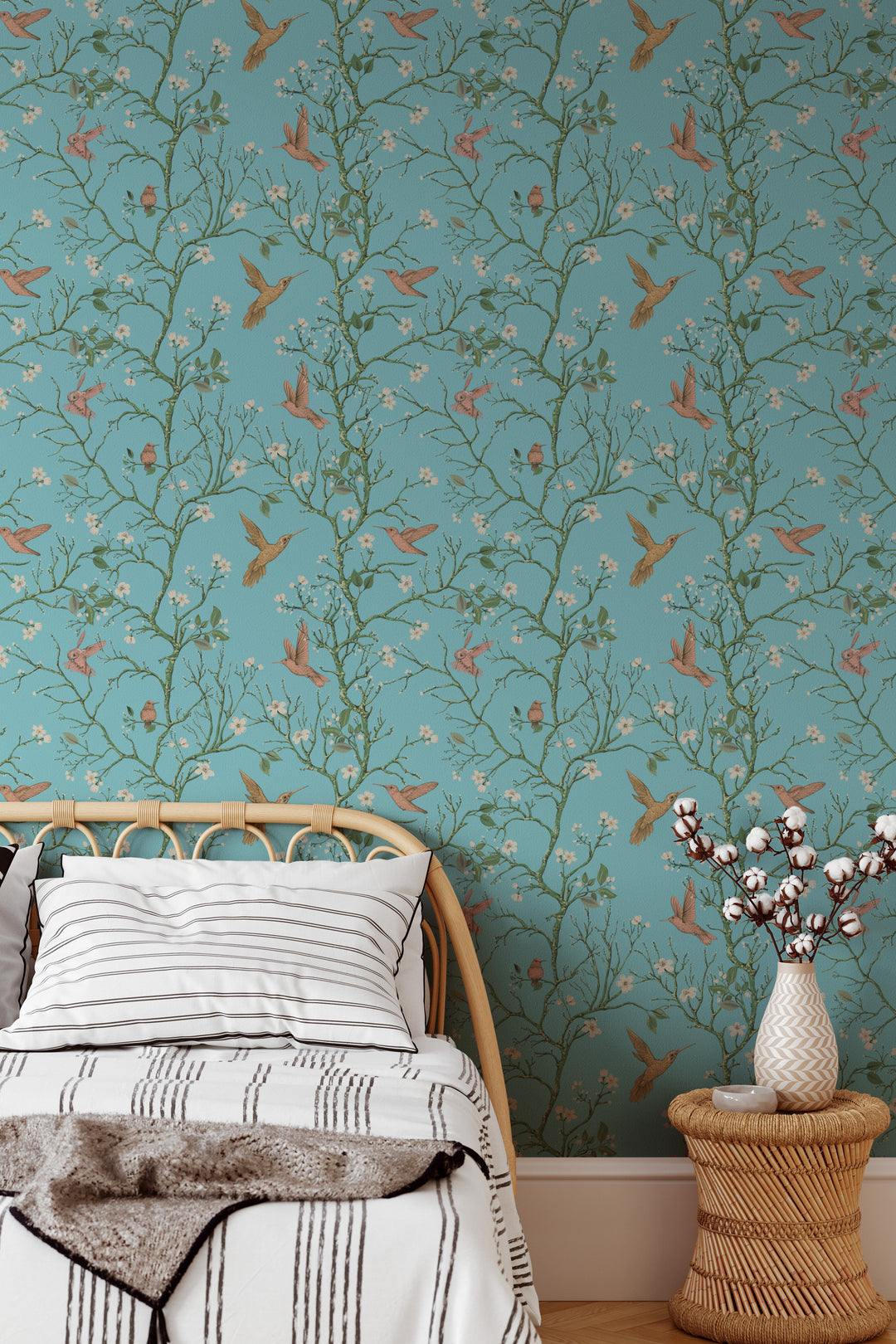 Aqua blue hummingbird wallpaper with flowering branches featured as a bedroom accent wall behind a rattan bed and side table.