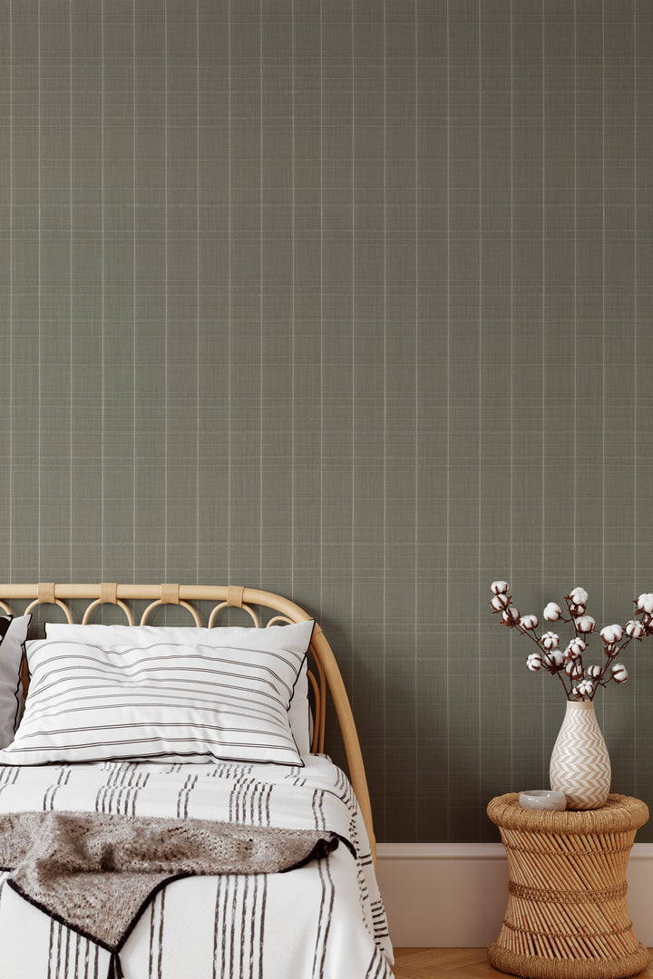 Sage gray Varrone canvas wallpaper with a subtle windowpane grid pattern behind a natural rattan bed frame, white striped bedding, and a woven bedside table with a decorative vase.