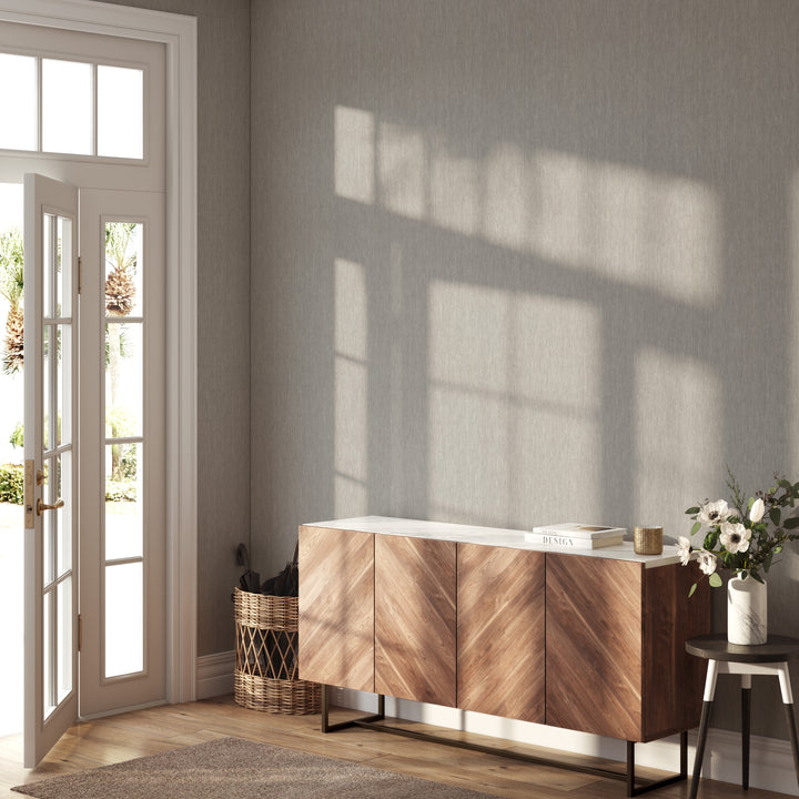 Light greige faux linen wallpaper with a subtle woven texture covering an entryway wall, paired with a warm wood sideboard, natural wood flooring, and soft sunlight streaming through an open door.