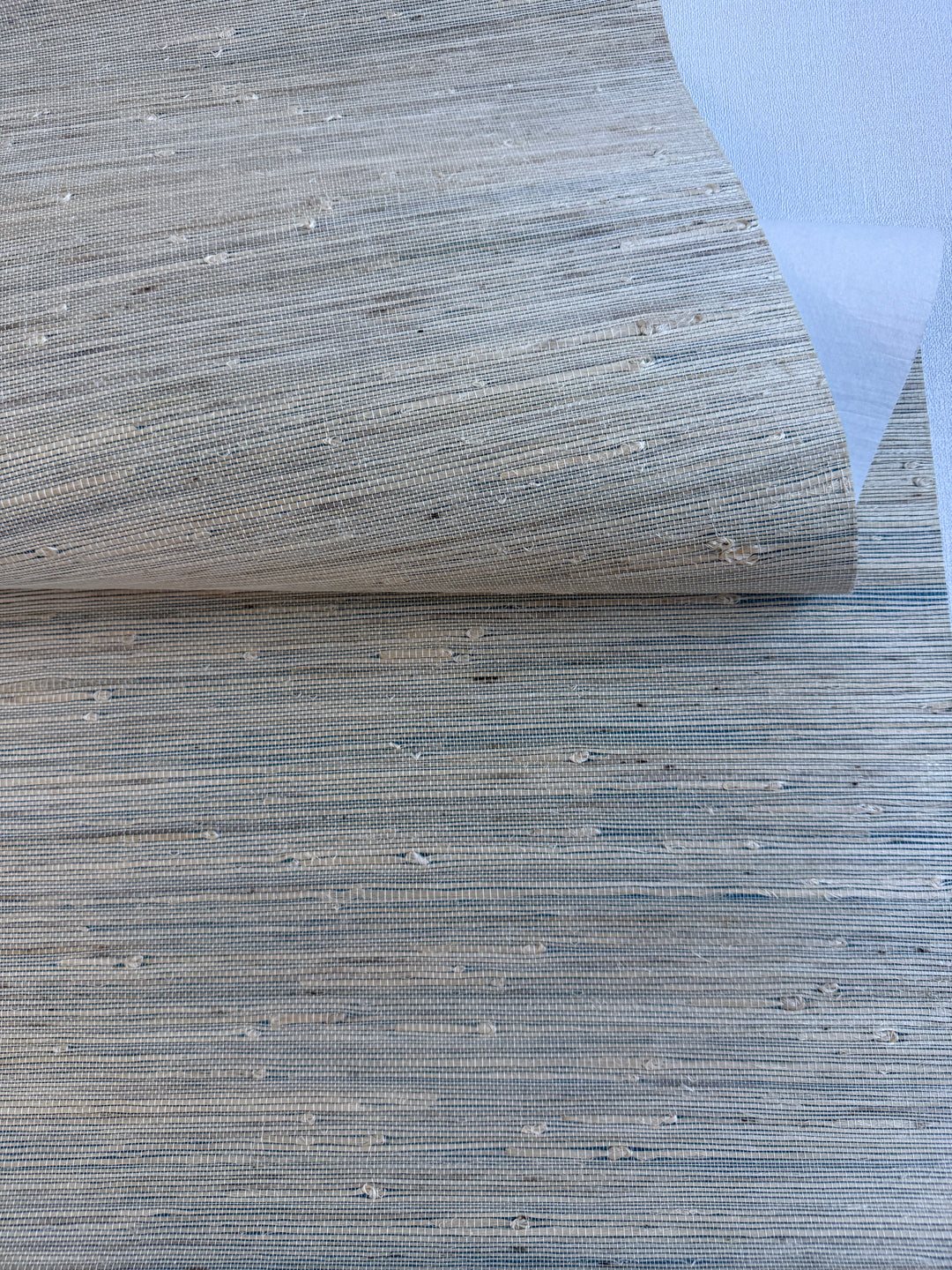 Handwoven Super Hemp natural grasscloth wallpaper in light beige with subtle blue undertone, close-up showing natural fiber knots and fine horizontal weave