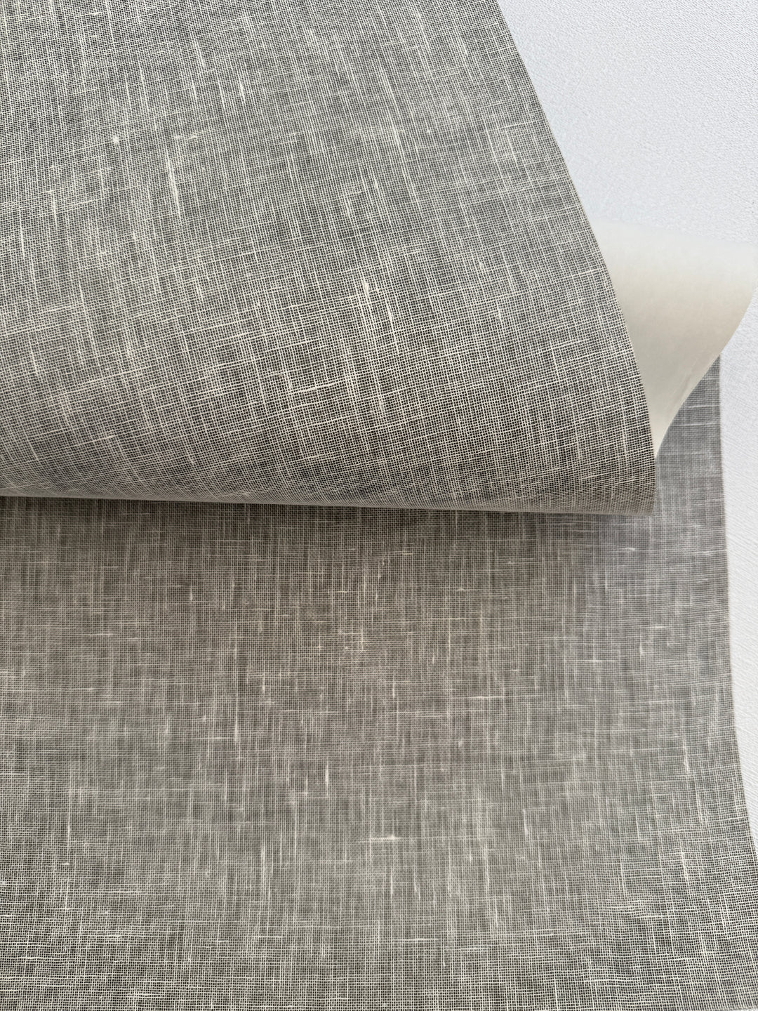 Handcrafted natural linen grasscloth wallpaper with light woven texture, close-up view showing real linen fibers and soft neutral tone