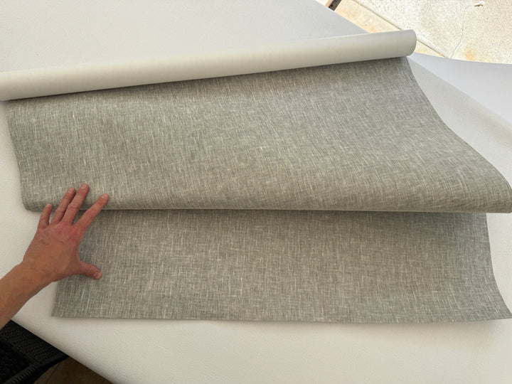 Person rolling out a roll of gray fabric on a white surface