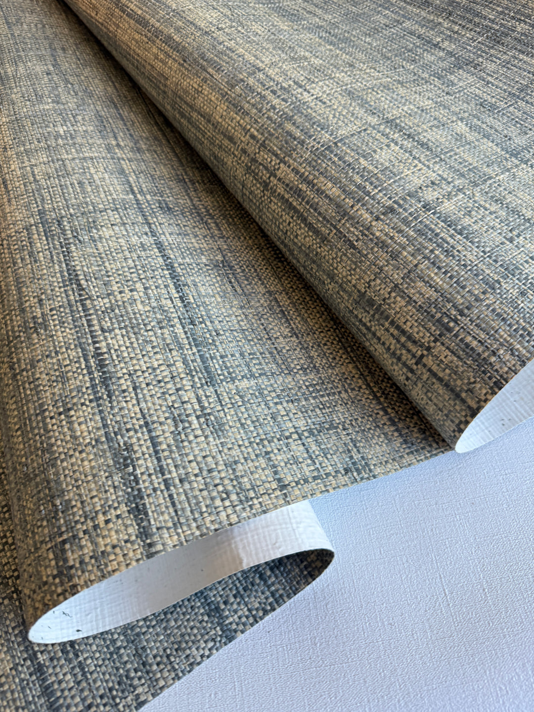 Roll of textured Raffia wallpaper with a neutral color palette on a light gray background