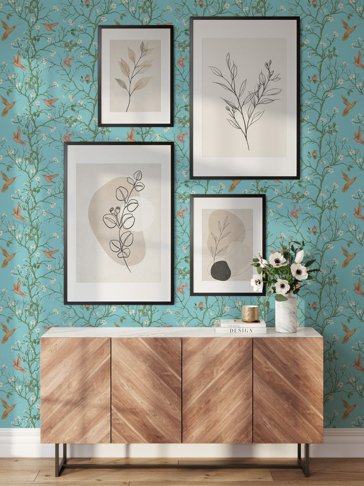 Aqua blue hummingbird wallpaper with flowering branches featured behind a wooden sideboard and framed botanical artwork in a stylish living room.