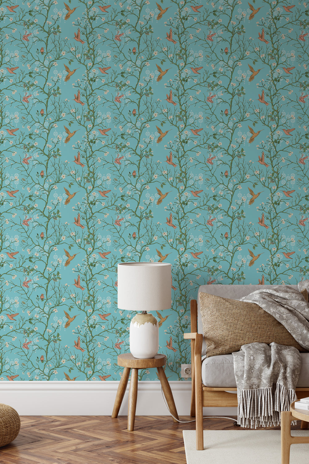 Aqua blue hummingbird wallpaper with delicate floral branches behind a cozy couch in a stylish living room.