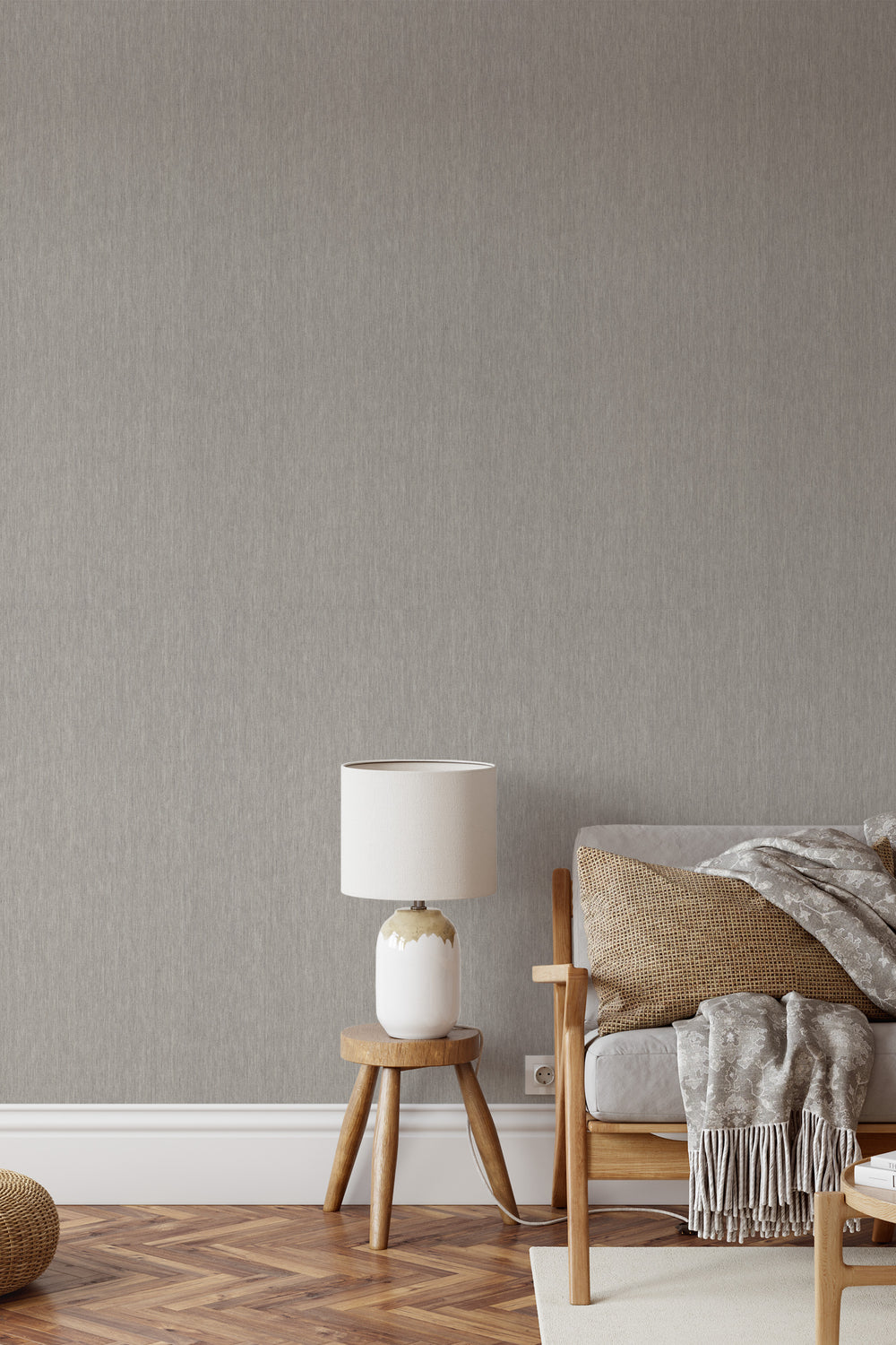 Light greige faux linen wallpaper with a subtle woven texture behind a wooden accent chair, neutral cushions, and a white ceramic table lamp in a cozy living room.