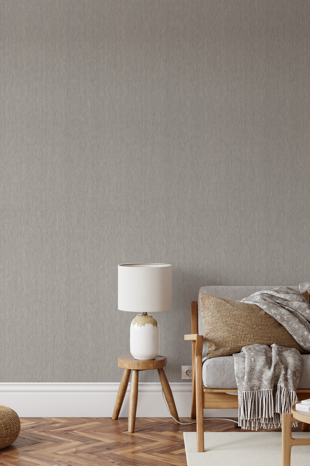 Light greige faux linen wallpaper with a subtle woven texture behind a wooden accent chair, neutral cushions, and a white ceramic table lamp in a cozy living room.