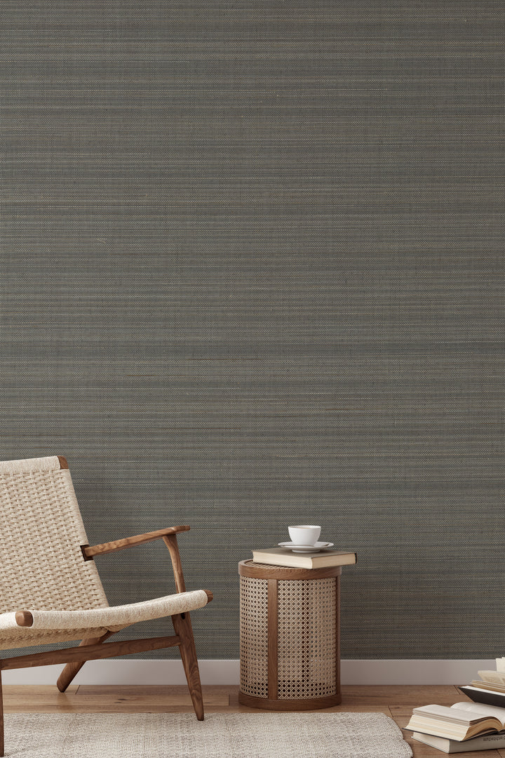 Woven wooden armchair with a book on soft gray-beige faux abaca grasscloth wallpaper.