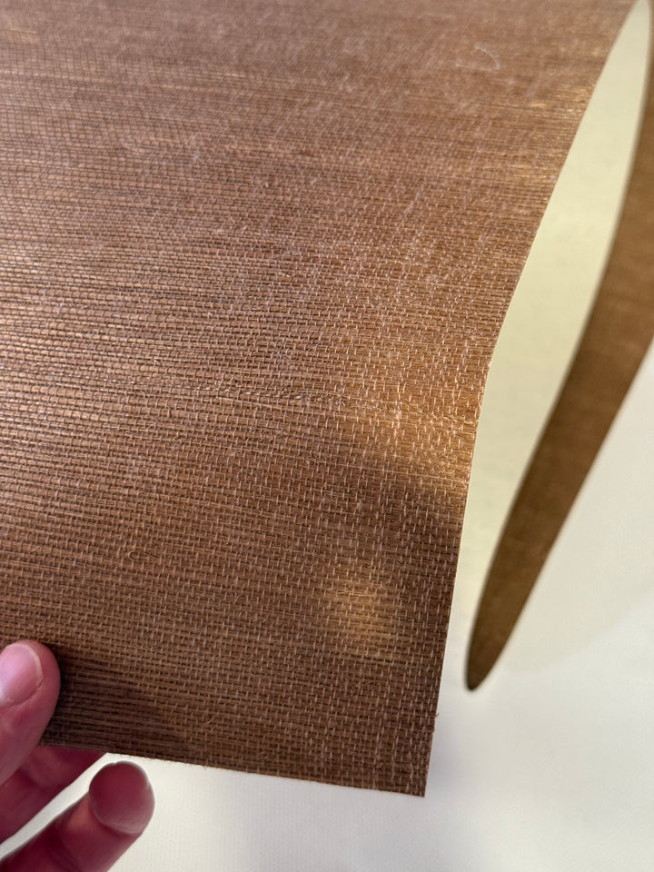 Brown textured fabric held by a hand against a white background