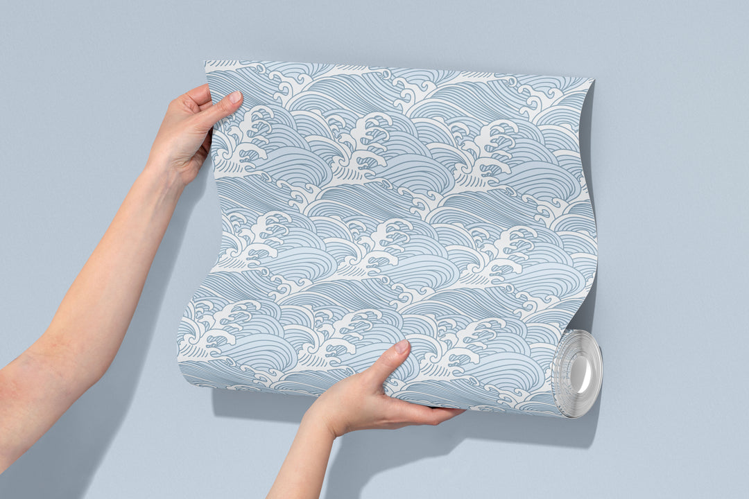 Hands holding a roll of cool blue Japanese wave wallpaper featuring a calm ocean pattern