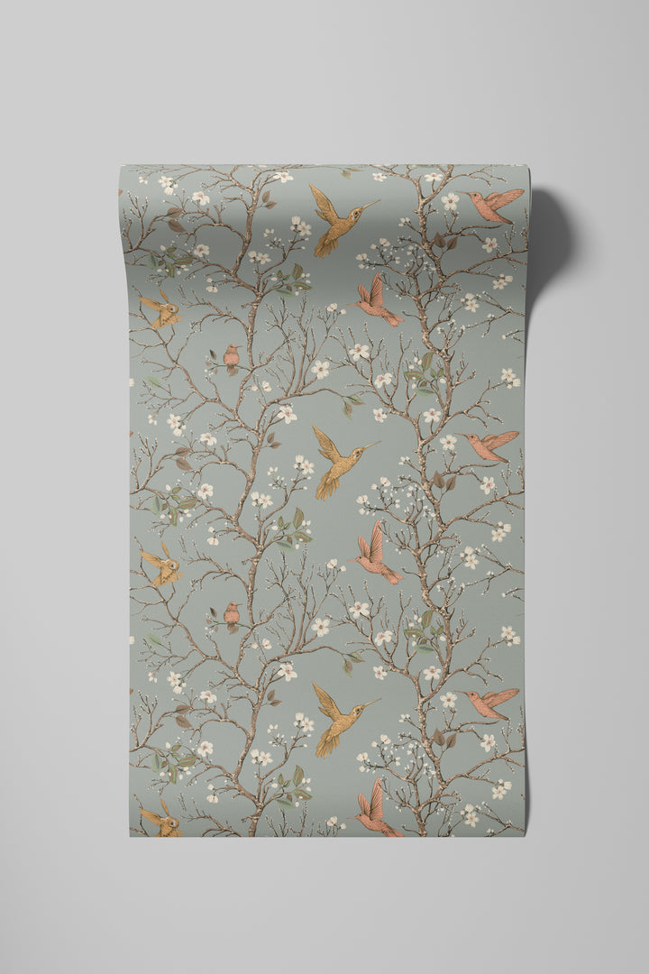 Sage gray hummingbird wallpaper with flowering branches and colorful birds displayed on a rolled wallpaper sample.