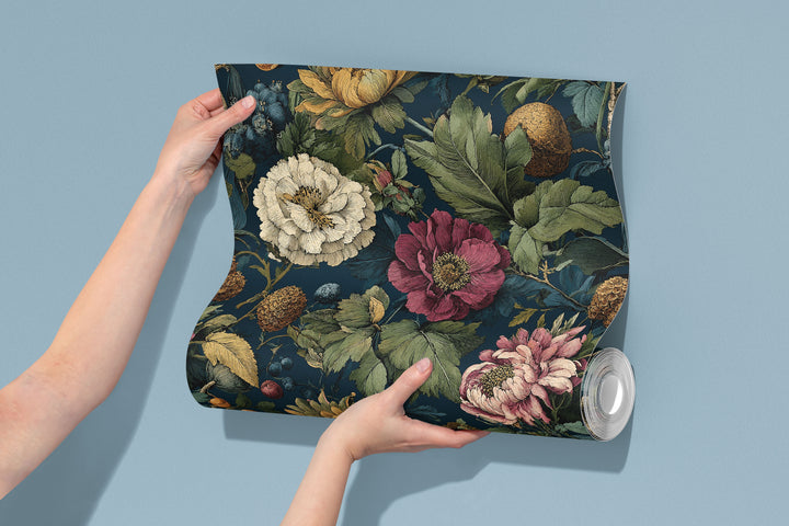 Dark teal vintage floral wallpaper with pink, cream, and yellow flowers, green leaves, and botanical foliage shown on a wallpaper roll