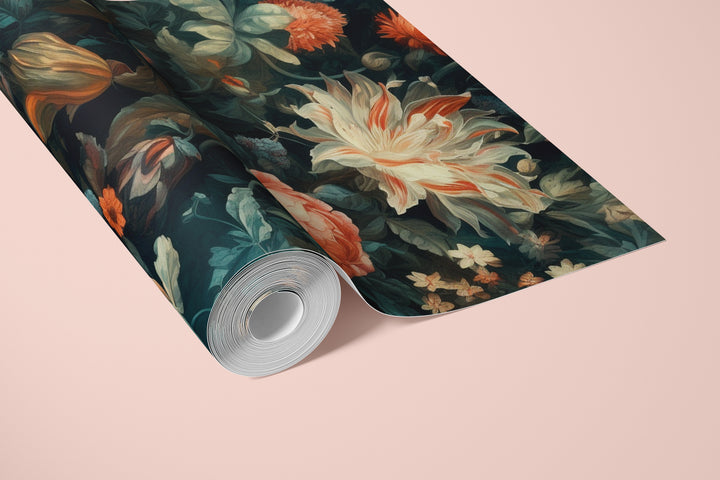 Cream and orange floral wallpaper on a dark teal background shown on a rolled wallpaper sample against a soft pink background.