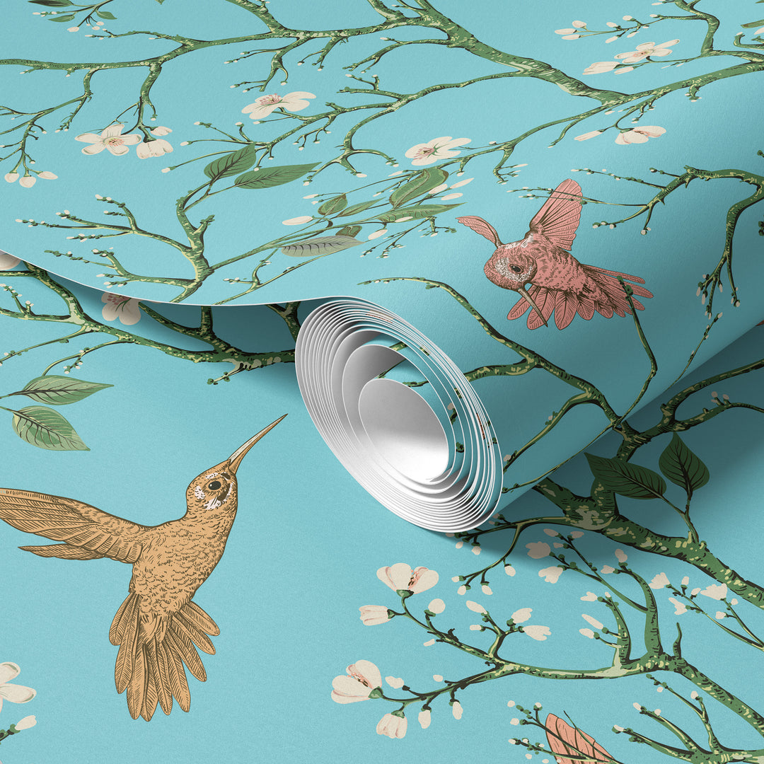 Aqua blue hummingbird wallpaper with flowering branches and colorful birds shown on a rolled wallpaper sample.