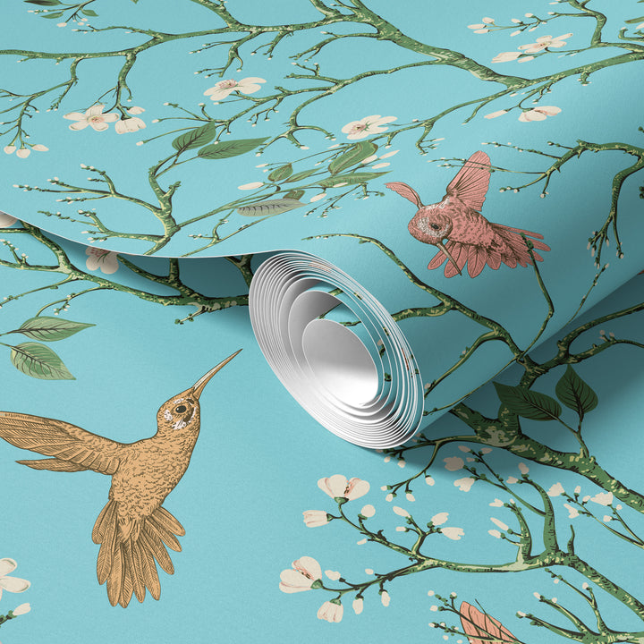 Aqua blue hummingbird wallpaper with flowering branches and colorful birds shown on a rolled wallpaper sample.