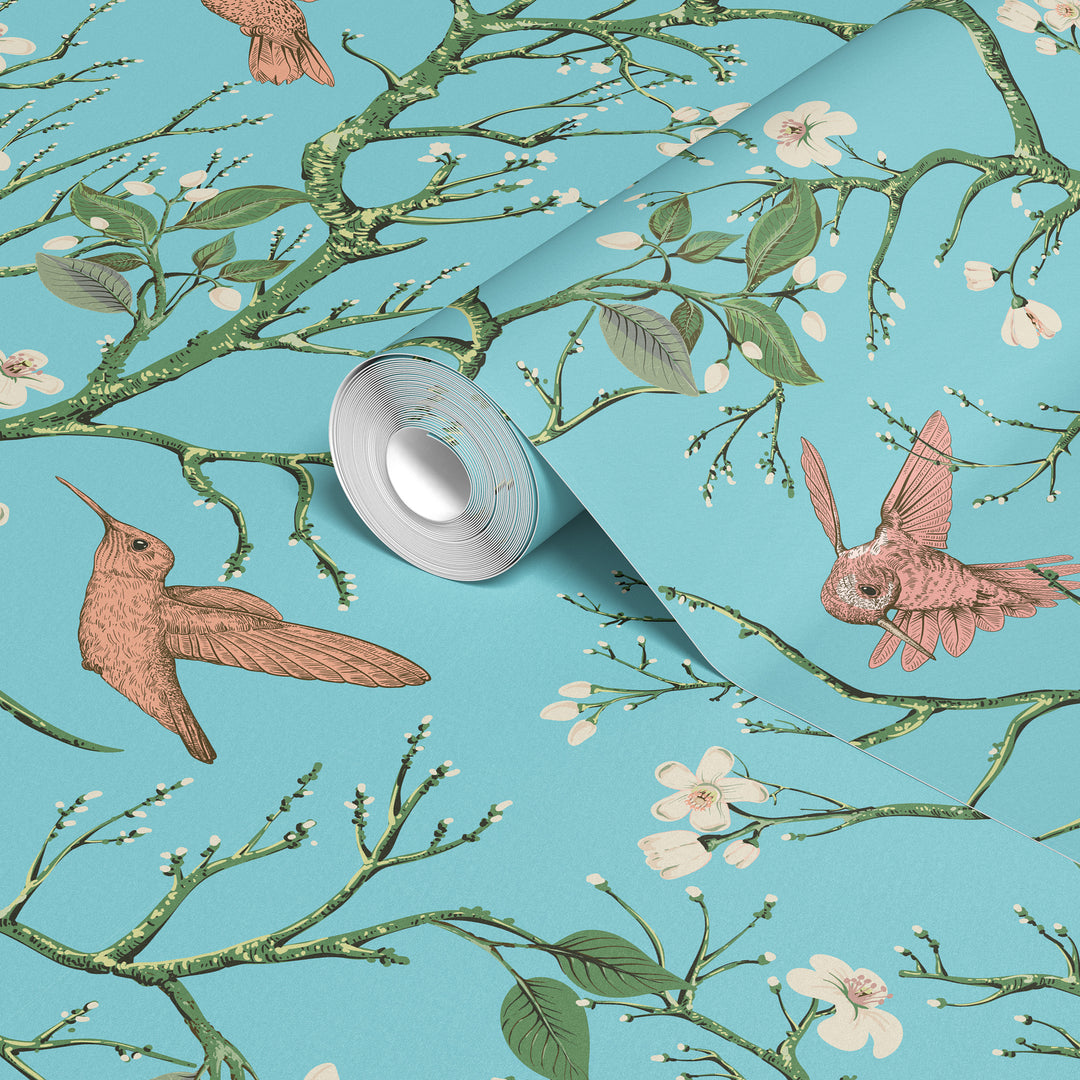 Aqua blue hummingbird wallpaper with flowering branches and colorful birds shown on a rolled wallpaper sample.