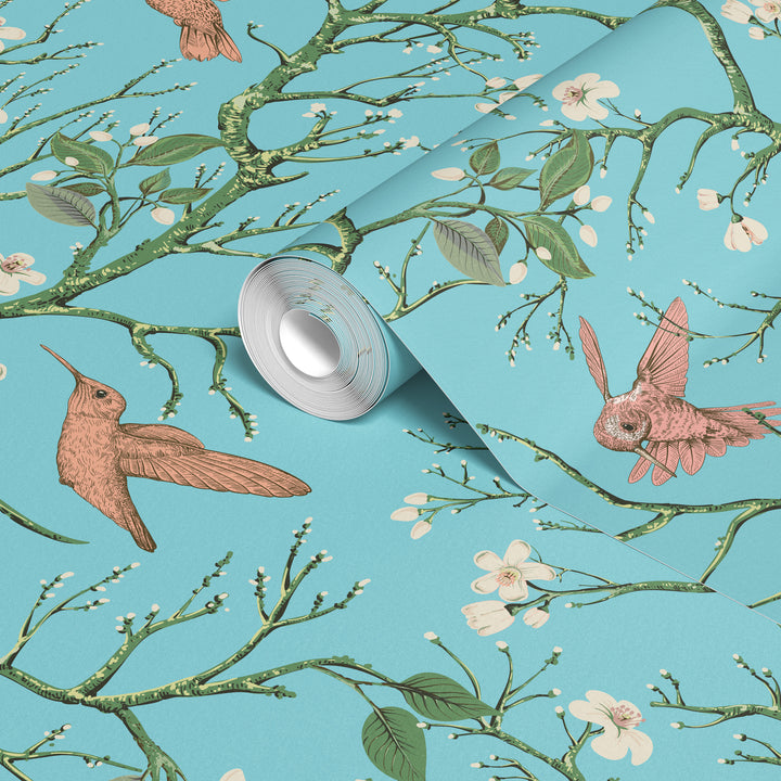 Aqua blue hummingbird wallpaper with flowering branches and colorful birds shown on a rolled wallpaper sample.