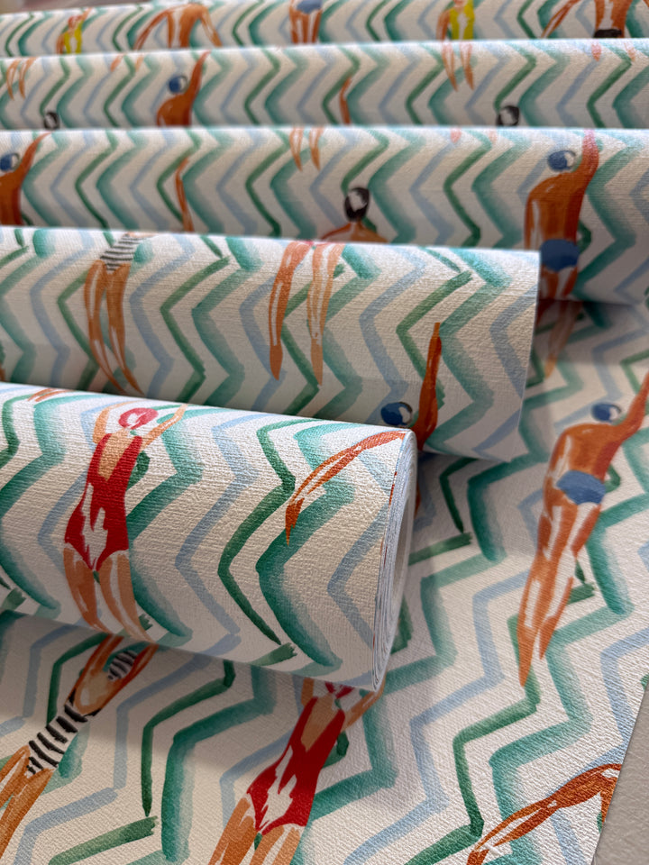 Rolled wallpaper with a retro watercolor pattern of figures swimming or dancing over a white background with teal and green chevron stripes.